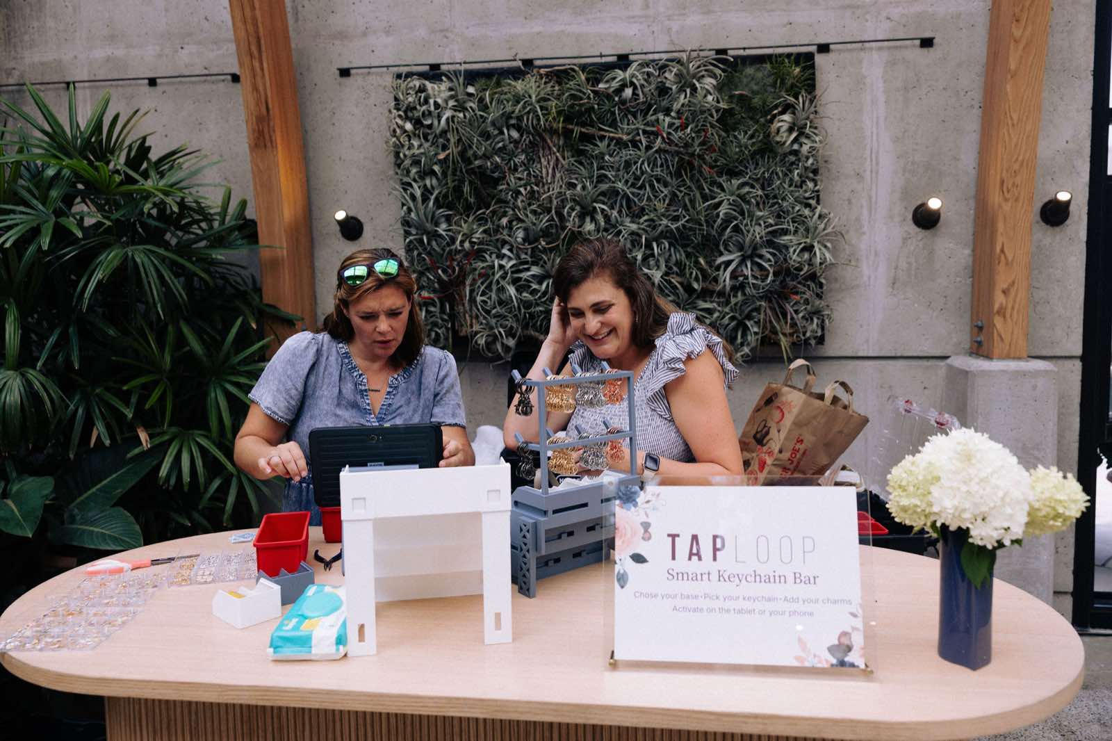 The TapLoop Smart Keychain Bar staffed and set up at the New England Botanical Garden — sign, keyring rack, and activation tablet ready for guests