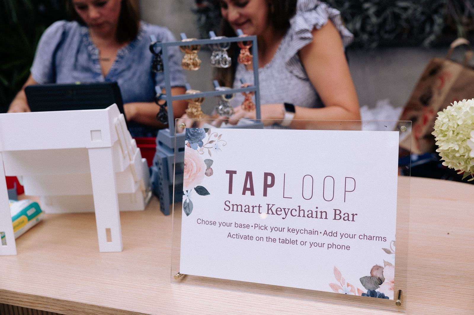 The TapLoop Smart Keychain Bar at a botanical garden event — guests picking charms behind the sign